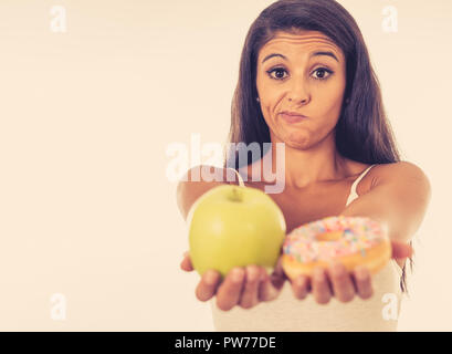 Schöne junge Frau versucht, die Wahl zwischen Apple und Krapfen in Gesund ungesunde Nahrung, Detox essen, Kalorien und Diät Konzept zu machen. Stockfoto