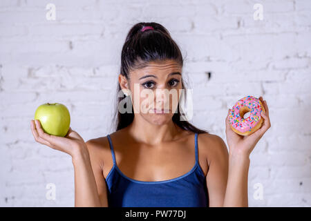 Schöne junge Frau versucht, die Wahl zwischen Apple und Krapfen in Gesund ungesunde Nahrung, Detox essen, Kalorien und Diät Konzept zu machen. Stockfoto