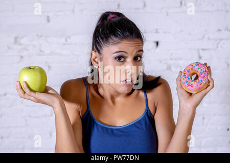 Schöne junge Frau versucht, die Wahl zwischen Apple und Krapfen in Gesund ungesunde Nahrung, Detox essen, Kalorien und Diät Konzept zu machen. Stockfoto