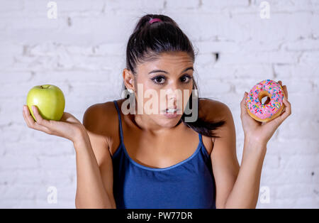 Schöne junge Frau versucht, die Wahl zwischen Apple und Krapfen in Gesund ungesunde Nahrung, Detox essen, Kalorien und Diät Konzept zu machen. Stockfoto