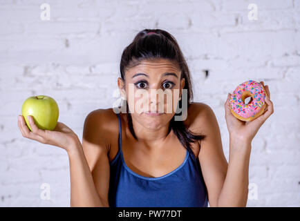 Schöne junge Frau versucht, die Wahl zwischen Apple und Krapfen in Gesund ungesunde Nahrung, Detox essen, Kalorien und Diät Konzept zu machen. Stockfoto