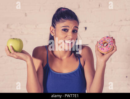 Schöne junge Frau versucht, die Wahl zwischen Apple und Krapfen in Gesund ungesunde Nahrung, Detox essen, Kalorien und Diät Konzept zu machen. Stockfoto