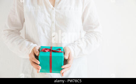 Junge kaukasier Frau hält in den Händen Geschenkbox im Grünbuch mit roter Schleife gebunden. Weißer Hintergrund Pastellfarben. Weihnachten Neue Jahre Valenti Stockfoto