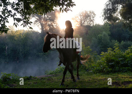 Junge Frau ein Pferd reiten auf eine schöne Landschaft. Klare See am Morgen Nebel. Sunrise Stockfoto
