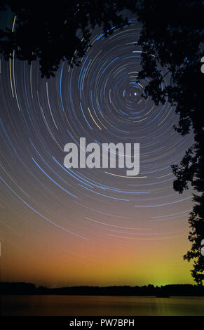 Lange Belichtung star Trails, Drehung um die North Star. Aurora Borealis leuchtenden grünen und roten über dem Horizont. Stockfoto