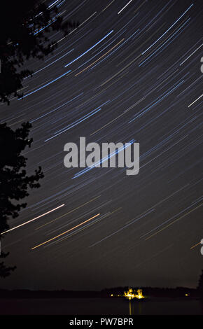 Lange Belichtung star trails Drehung um die North Star. Ferienhaus Lichter im Horizont. Stockfoto