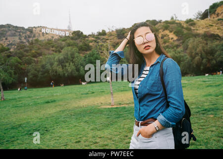 Elegante Hündin touristische Stehend auf dem Gras, Stylen ihr Haar mit dem berühmten Hollywood Schild im Hintergrund. Freudige traveler Walking im Freien in Stockfoto