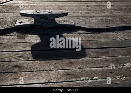 Ein Liegeplatz auf dem Deck eines alten hölzernen Boot wirft einen Schatten bei schlechten Lichtverhältnissen. Stockfoto