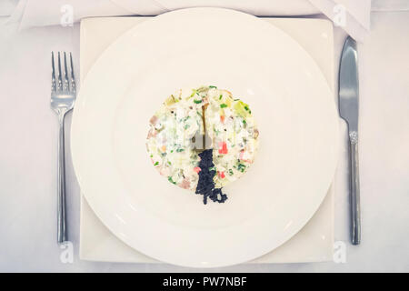 Cremige elegante Salat mit Kaviar in Weiß Platte am weißen Tisch mit von oben nach unten anzeigen. Restaurant mit. Restaurant Dish in einem Teller mit Messer ein Stockfoto
