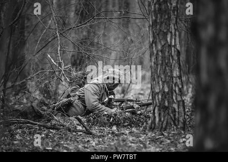 Versteckte unbekannte Re-Enactor gekleidet, wie Deutsche Wehrmacht Soldat ein Gewehr auf gegnerische vom Boden zum Ziel haben. Foto in den Farben Schwarz und Weiß. Stockfoto