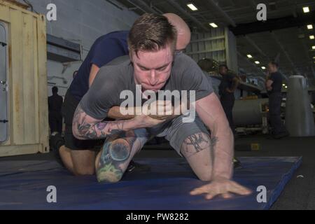 ARABIAN GULF (Okt. 2010) 2, 2017) Air Traffic Controller 2. Klasse Brandon Reyes, von Panama City, Fla., ringt mit Air Traffic Controller 3. Klasse Kenneth Taggart, aus Atlanta, im Hangar Bucht der Flugzeugträger USS Nimitz (CVN68) für körperliches Training. Der Nimitz ist derzeit in den USA 5 Flotte Bereich der Operationen zur Unterstützung der Operation inhärenten Lösung bereitgestellt. Während in der Region, das Schiff und Streik Gruppe leiten Maritime Security Operations Verbündeten und Partnern zu beruhigen, die Freiheit der Schifffahrt zu bewahren und den freien Fluss des Handels halten. Stockfoto