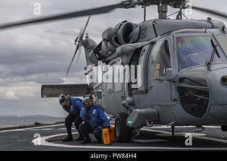 Irische See (Okt. 2010) 3, 2017) der Bootsmann Mate 2. Klasse Shadi Azhari Signale einem MH-60 Sea Hawk Hubschrauber zum "Ladegeräte" der Hubschrauber Meer Combat Squadron (HSC) 26 an Bord der Arleigh-Burke-Klasse geführte Anti-raketen-Zerstörer USS Donald Cook (DDG75) während der Übung gemeinsame Krieger 17-2. Großbritannien-led, multinationale Übung entwickelt die Interoperabilität und die Zusammenarbeit in allen Bereichen anwendbar Kriegsführung. Stockfoto