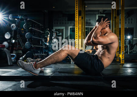 Muskulöse Kerl, Sit Ups im Fitnessstudio mit anderen Menschen im Hintergrund. Junge Sportler tun Magen trainieren Sie im modernen Fitnessraum. Schön fit Mann crunches machen Stockfoto