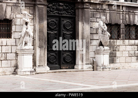 Schwarze Tür in der Fassade eines alten Gebäudes mit weißem Marmor Steine und zwei Statuen auf den Seiten