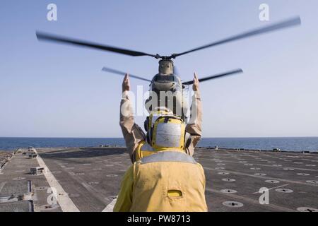 5. Flotte EINSATZGEBIET (Okt. 2010) 2, 2017) Marine Cpl. Ryan Carr, ein Eingeborener von Oceanside, Kalifornien, zu der Bekämpfung Cargo Abteilung an Bord der Amphibischen dock Landung Schiff USS Pearl Harbor (LSD 52), unterstützt von Seaman Miguel Mendez (vorne), ein Eingeborener von Orlando zugewiesen ist, leitet ein CH-47D Chinook, zugeordnet zu den Armee Bravo Company, 2.BATAILLON, 149 Allgemeine Unterstützung Aviation Battalion (Gsab), wie es landet auf dem Schiff Flight Deck. Pearl Harbor ist Teil der Amerika Amphibious Ready Group (ARG) und, mit dem begonnen 15 Marine Expeditionary Unit (MEU), ist zur Unterstützung der maritimen Secu bereitgestellt Stockfoto