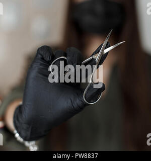 Nagelschere. Frau in Schwarz Handschuhe hält die Schere. Nagelpflege Stockfoto