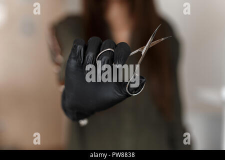 Weibliche Hände in einem schwarzen Handschuh halten eine Nagelschere. Nail Care Concept Stockfoto