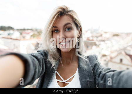 Überrascht lustig schöne junge Frau mit einem Lächeln in einem vintage Anzug tun selfie auf Kamera in die Stadt. Girl blogger reist in die Stadt und schießt Stockfoto