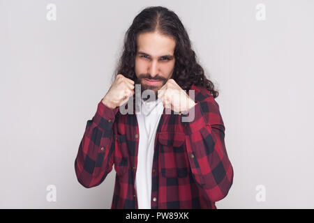 Porträt von Ernst stattlicher Mann mit Bart und schwarzen langen Locken in der beiläufigen kariert rot Shirt stehend, auf Kamera und zum Angriff bereit. Stockfoto