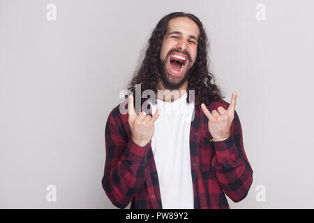 Rock und Roll. lustiger Mann mit Bart und schwarzen langen Locken in der beiläufigen kariert rot shirt Suche ar Kamera mit Rock zeichen Geste und Schreien. Stockfoto