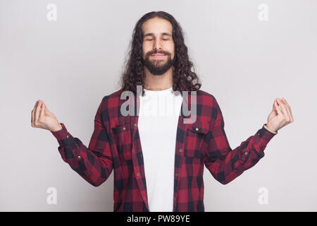 Portrait von ruhigen meditativen stattlicher Mann mit Bart und schwarzen langen Locken im lässigen Stil, kariert rot Shirt mit clossed Augen und Yoga Stockfoto