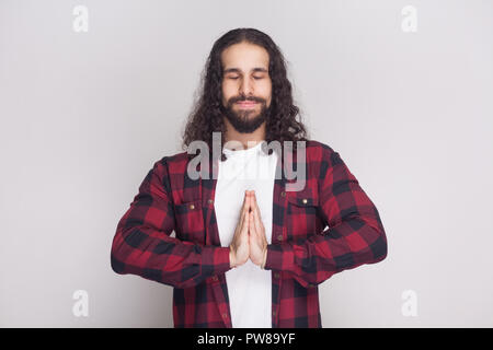 Portrait von ruhigen meditativen stattlicher Mann mit Bart und schwarzen langen Locken im lässigen Stil, kariert rot Shirt mit clossed Augen und Yoga Stockfoto
