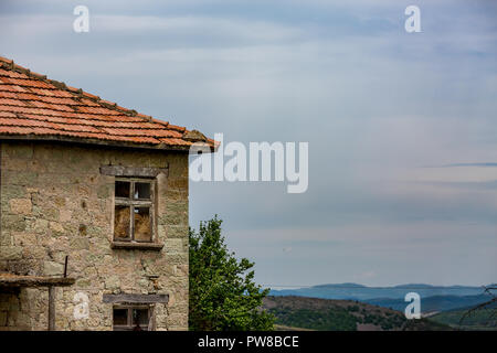 Alten, verlassenen geknackt Granit Stein Haus mit roten Dachziegeln in Scheune steht unter dem hohen Kontrast frühling himmel der Rhodopen, Bulgari Stockfoto
