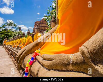 Thailand, beeindruckende Reihe von Buddha Statuen mit orangefarbenen Roben in Ayutthaya alte Tempel - Detail einer Hand eine Blume whreat Stockfoto