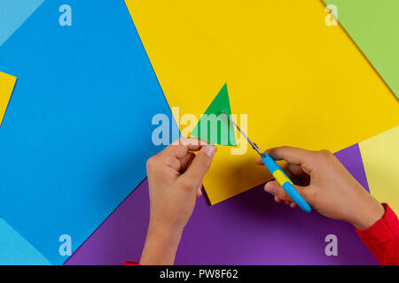 In der Nähe der Hände des Kindes schneiden Weihnachtsbaum von farbigem Papier handgefertigte Neues Jahr Dekorationen oder Karte vorzubereiten. Stockfoto