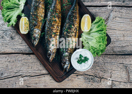 Ein lecker gebratene Makrele auf einem Grill, auf einem Holzbrett vorgestellt, und entlang der Blätter von grüner Salat und Stücke von Zitrone. Stockfoto