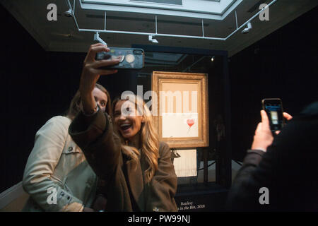 London, Großbritannien. 14. Oktober 2018. Besucher die selfies vor banksys "Liebe im bin", die in der Öffentlichkeit bei Sothebys in New Bond Street in London. Die Kunstwerke, die früher als "Das Mädchen mit einem Ballon" bekannt wurde geschreddert Momente nach dem Zuschlag und der Hammer fiel bei Auktion an einen ausländischen Käufer am 5. Oktober Credit: Amer ghazzal/Alamy Live News Credit: Amer ghazzal/Alamy leben Nachrichten Stockfoto