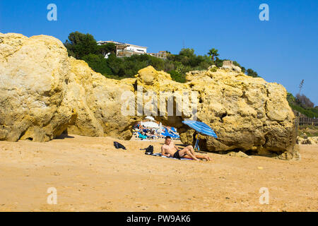 29. September 2018 ein Paar in der Sonne sitzen neben eine kleine Sonne brolly auf einem entfernten Teil der Oura Praia in Albferiah an der Algarve in Portugal Stockfoto