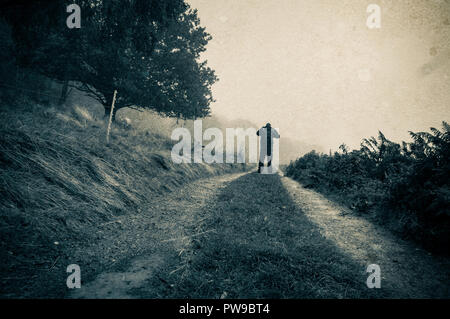Eine einsame Silhouette einer Abbildung auf einem nebligen Pfad in der Landschaft mit einem Oldtimer, grunge Duo Tone bearbeiten Stockfoto