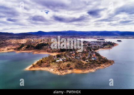 Jindabyne Stadt am Ufer des Lake Jindabyne See im Winter mit fernen Berggipfeln der schneebedeckten Berge von Schnee unter bewölktem Himmel bedeckt mit lokalen befinden Stockfoto