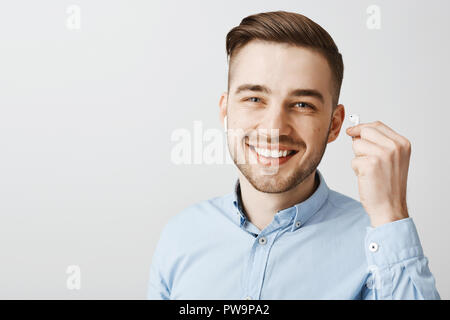 Nahaufnahme der glücklichen optimistisch und freundlicher junger hübscher Kerl mit schönen Lächeln und Borsten, die Drahtlose Ohrhörer in Beantwortung der Frage von Hören Favorite Track unterbrochen wird Stockfoto