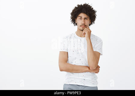 Verdächtige ernst - auf der Suche netten Hispanic männliches Modell im casual Outfit, runzelte die Stirn und halten Sie den Finger auf die Lippen und schielen, während zweifelnd, den Blick mit Unglauben an Freund, der Lügen Stockfoto