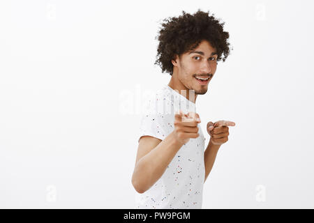 Hey, was ist. Freundlich und schön zuversichtlich männlichen Freund mit dunkler Haut und Afro Frisur steht im Profil, lächelnd und zeigte mit fingergun Geste an Kamera, Gruß Gehilfen zu Hause Stockfoto