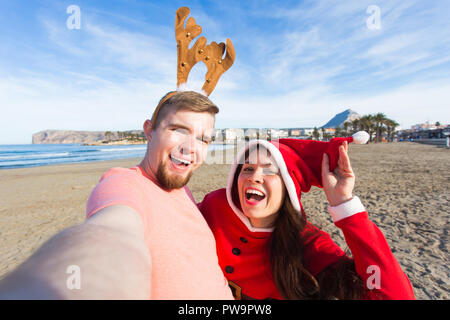 Spaß und Winterurlaub Konzept - glückliches Paar in Weihnachten Kostüme unter selfie über Sandstrand Hintergrund Stockfoto