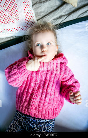 Blue-eyed süße Mädchen in einem rosa Pullover denkt Stockfoto