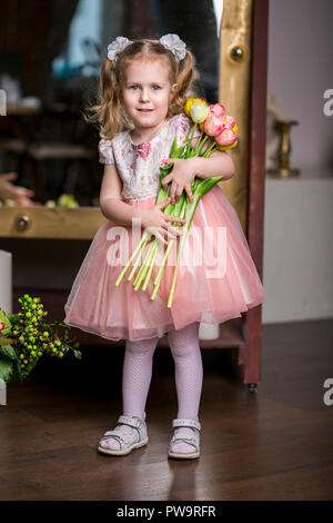 Blue-eyed niedliche Mädchen in ein rosa Kleid halten in ihren Händen einen Armful Tulpen Stockfoto