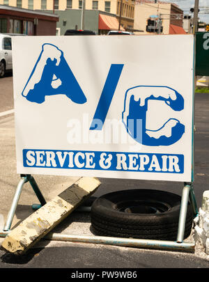 Ein weißes Schild sagt AC Service und Reparatur, die von einem Strahl und Reifen gewichteten Stockfoto