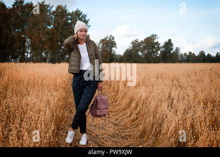 Portrait fröhliche junge Frau mit Brünette Haar in Strick Hut, grünen Mantel und t-shirt Spaß, lächeln und genießen Sie Tag auf dem Feld. Stilvolle hipster woma Stockfoto