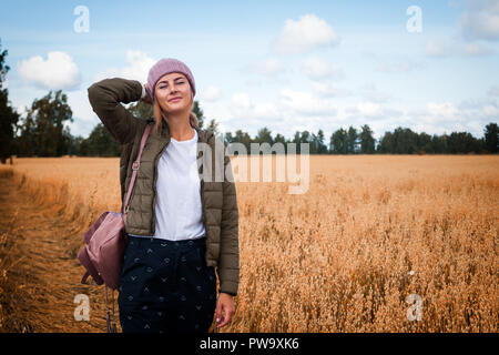 Portrait fröhliche junge Frau mit Brünette Haar in Strick Hut, grünen Mantel und t-shirt Spaß, lächeln und genießen Sie Tag auf dem Feld. Stilvolle hipster woma Stockfoto