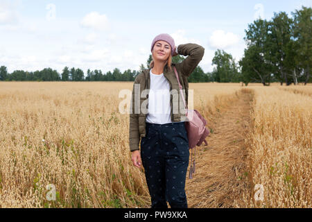 Portrait fröhliche junge Frau mit Brünette Haar in Strick Hut, grünen Mantel und t-shirt Spaß, lächeln und genießen Sie Tag auf dem Feld. Stilvolle hipster woma Stockfoto