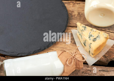 Milchprodukte auf Holz- Hintergrund. Flasche mit Milch, Sauerrahm, französischer Roquefortkäse und Schiefer Board auf rustikalen, mit Holz. Gesunde Milch essen. Stockfoto