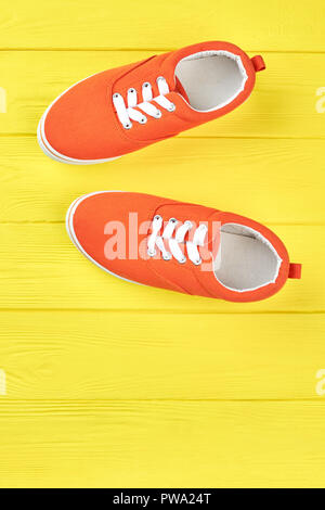 Weibliche Sneakers auf gelben Hintergrund. Orange Sport Schuhe mit Schnürsenkel auf hölzernen Hintergrund und Kopieren. Frau Sommer Schuhe. Stockfoto