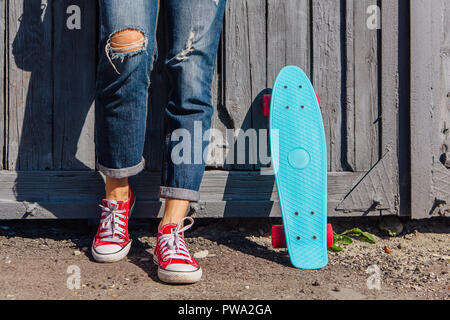 Close up Füße eines Mädchens in rote Turnschuhe und Blue Penny Skate Board mit rosa Räder neben der Wand stehen. Städtische Szene, Leben in der Stadt. Sport, Fitness Stockfoto