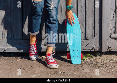 Close up Füße eines Mädchens in rote Turnschuhe und Blue Penny Skate Board mit rosa Räder neben der Wand stehen. Städtische Szene, Leben in der Stadt. Sport, Fitness Stockfoto