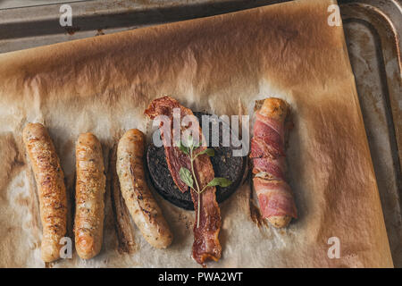 Gebratene Würstchen, Speck, Blutwurst aus dem Backofen auf braun Backpapier Hintergrund Stockfoto