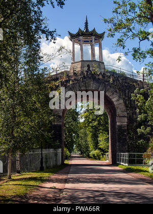 Oberhalb der Straße mit üppigen Bäumen am Straßenrand Türmen eine steinerne Brücke Tunnel mit einem chinesischen Stil sommerhaus auf der Oberseite im Sommer an einem sonnigen Tag in Tsa Stockfoto